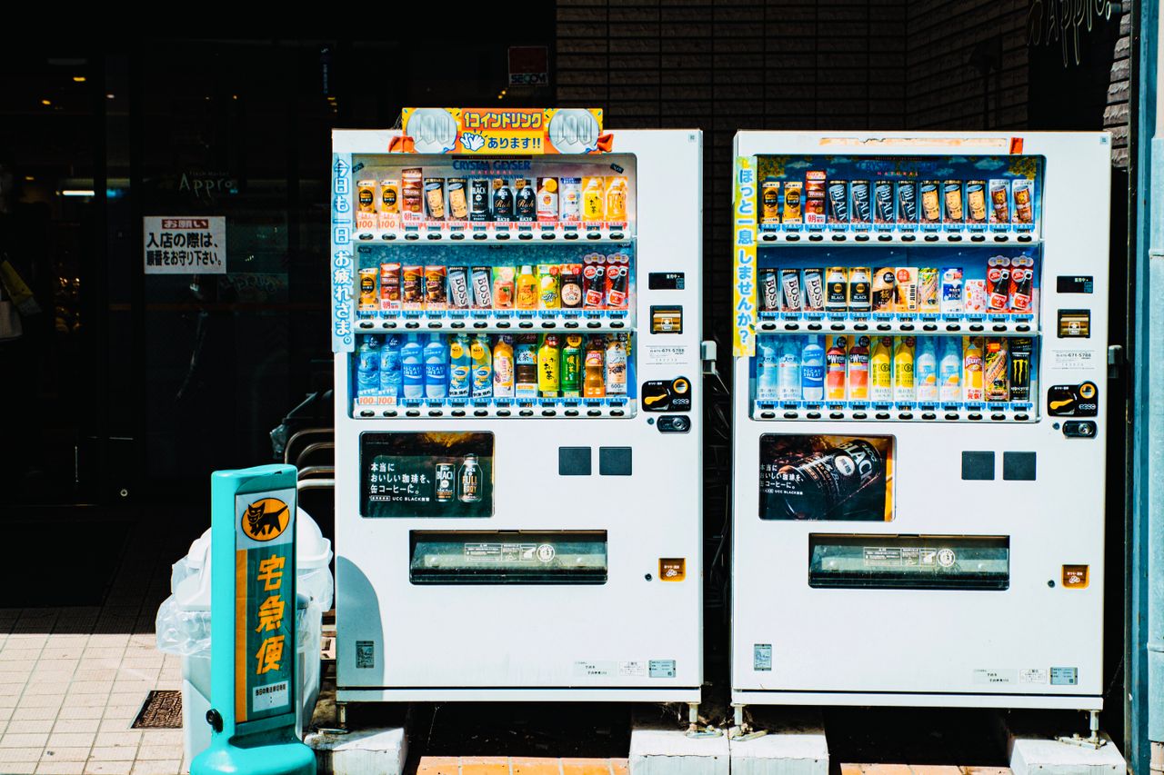 menu-11 Colorful array of beverages in Japanese vending machines on a sunny city street.