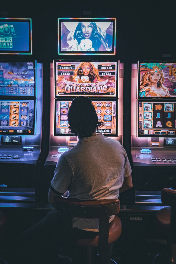 about-01 Adult male seated in a dimly lit casino engaging with vibrant slot machines at night.